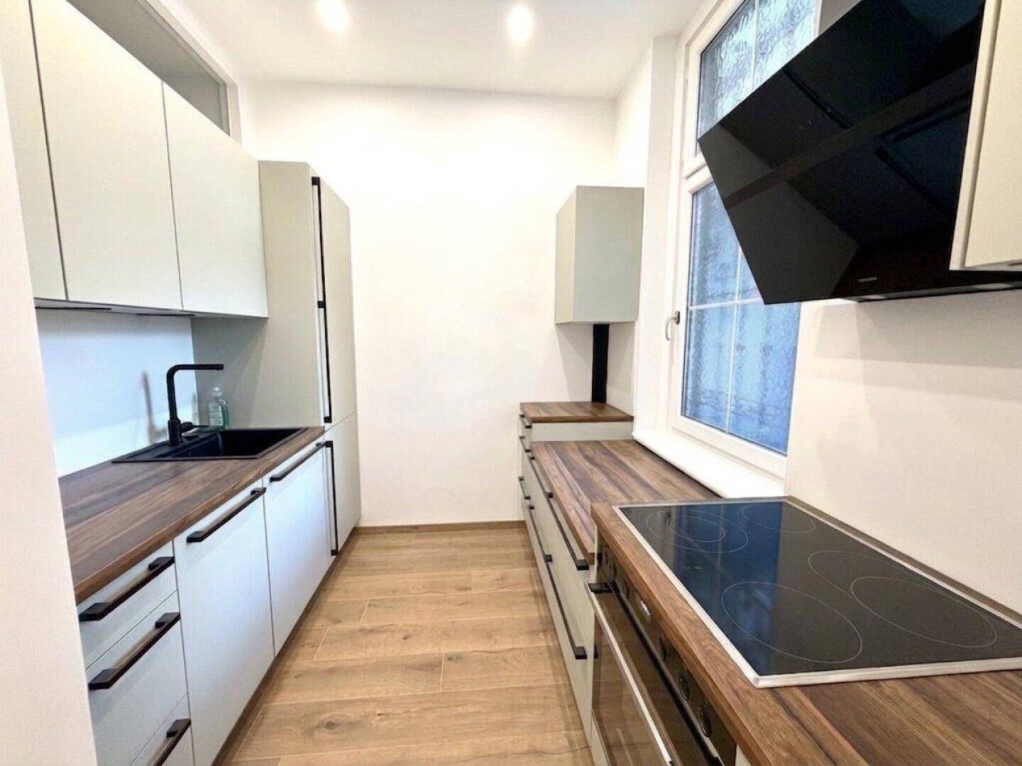 Moderne Küche mit weißen Schränken, Holz-Arbeitsplatten, Induktionskochfeld und Dunstabzugshaube.