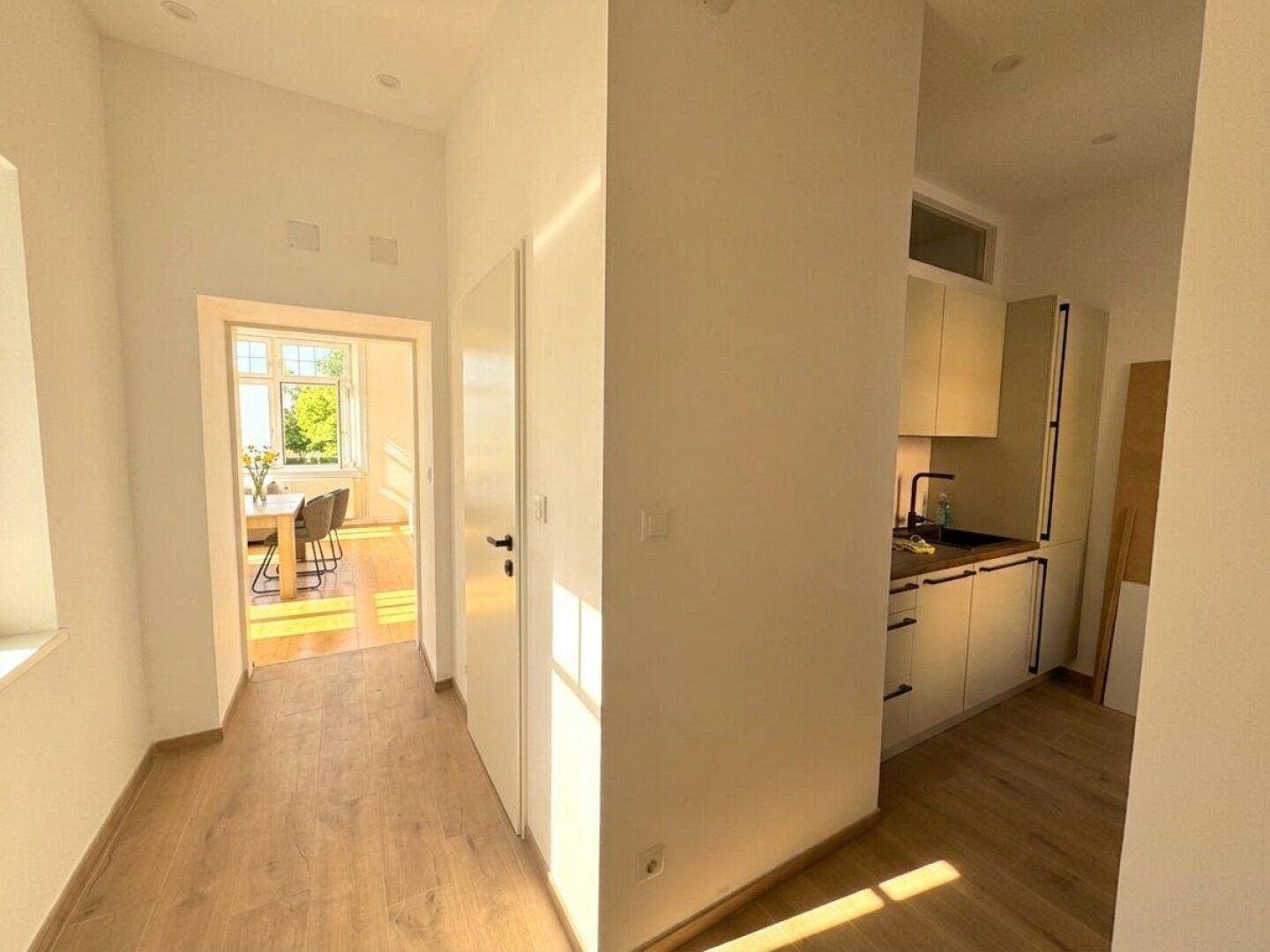 Heller Flur mit Holzboden, der zu einem weiteren Raum und einer modernen Küchenzeile führt.