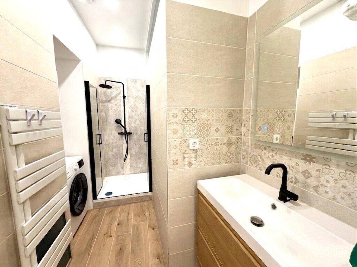 Modernes Badezimmer mit begehbarer Dusche, Waschbecken, beheiztem Handtuchhalter und Waschmaschine.