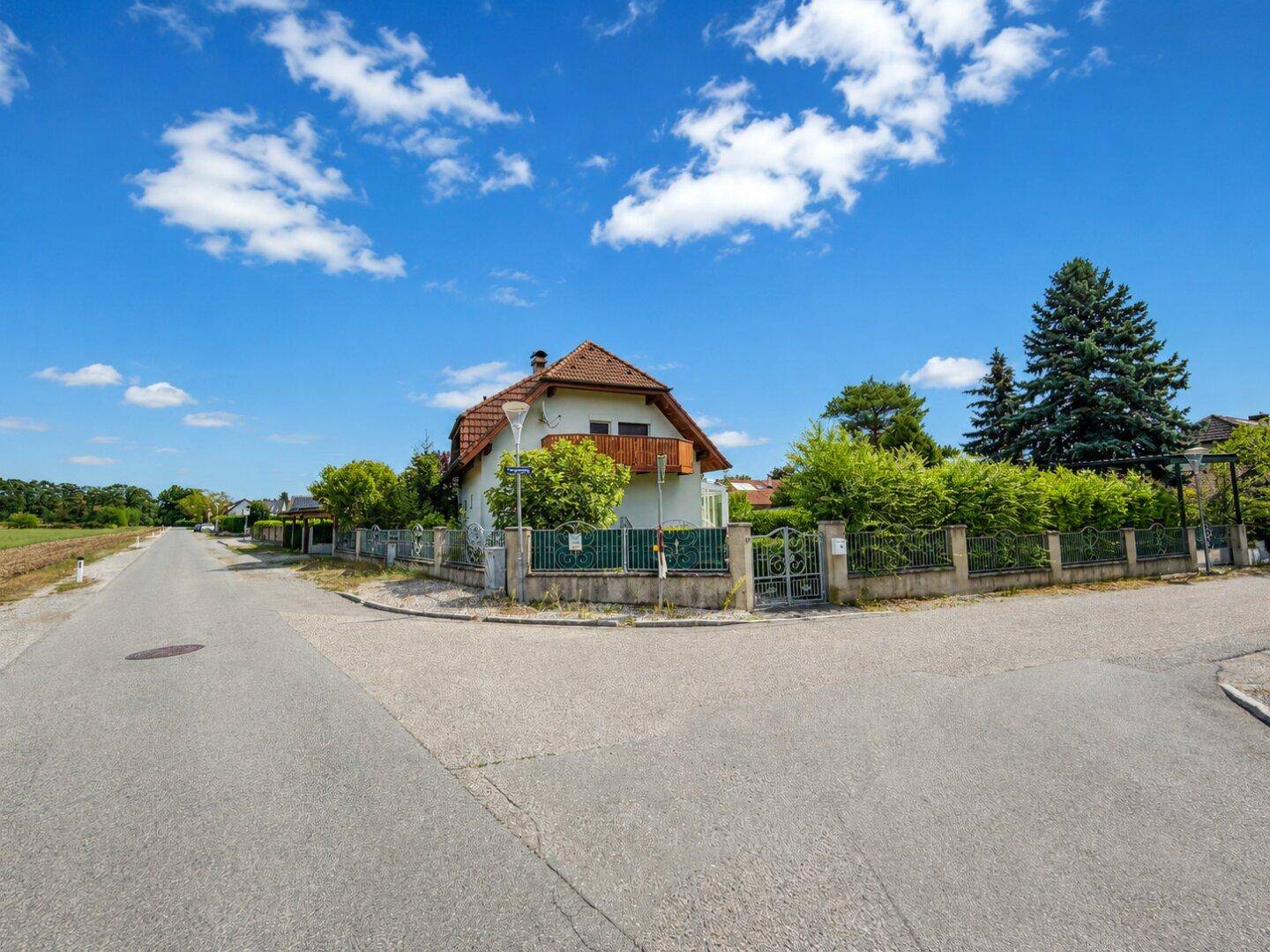 Ansicht des Hauses von der Straße mit Zaun und umgebender ländlicher Bebauung.