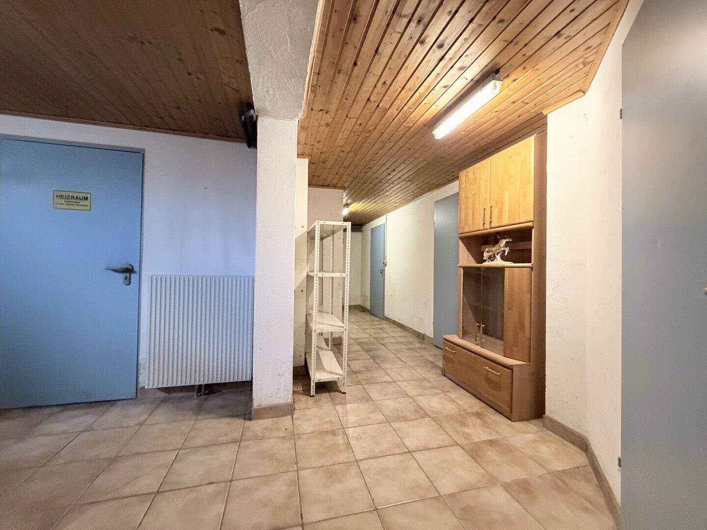 Kellerflur mit Fliesenboden, Holzdecke und Zugang zu verschiedenen Kellerräumen.