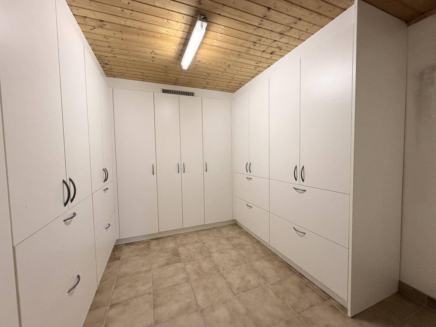 Großer Abstellraum im Keller mit vielen weißen Einbauschränken und Fliesenboden.