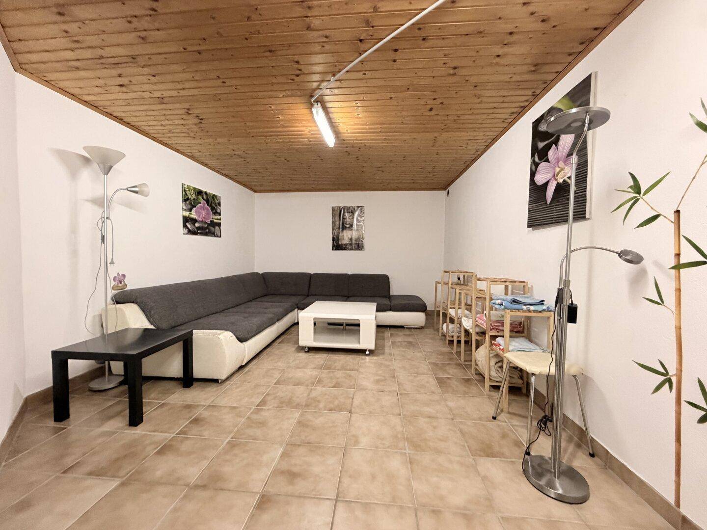 Ausgebauter Kellerraum mit Fliesenboden, Holzdecke und großem Ecksofa als Wohnbereich.