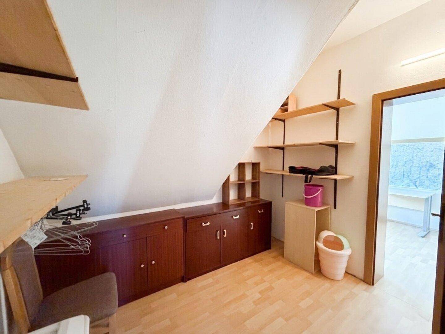 Dachgeschossraum mit Dachschräge, Laminatboden und praktischen Regalen für Stauraum.