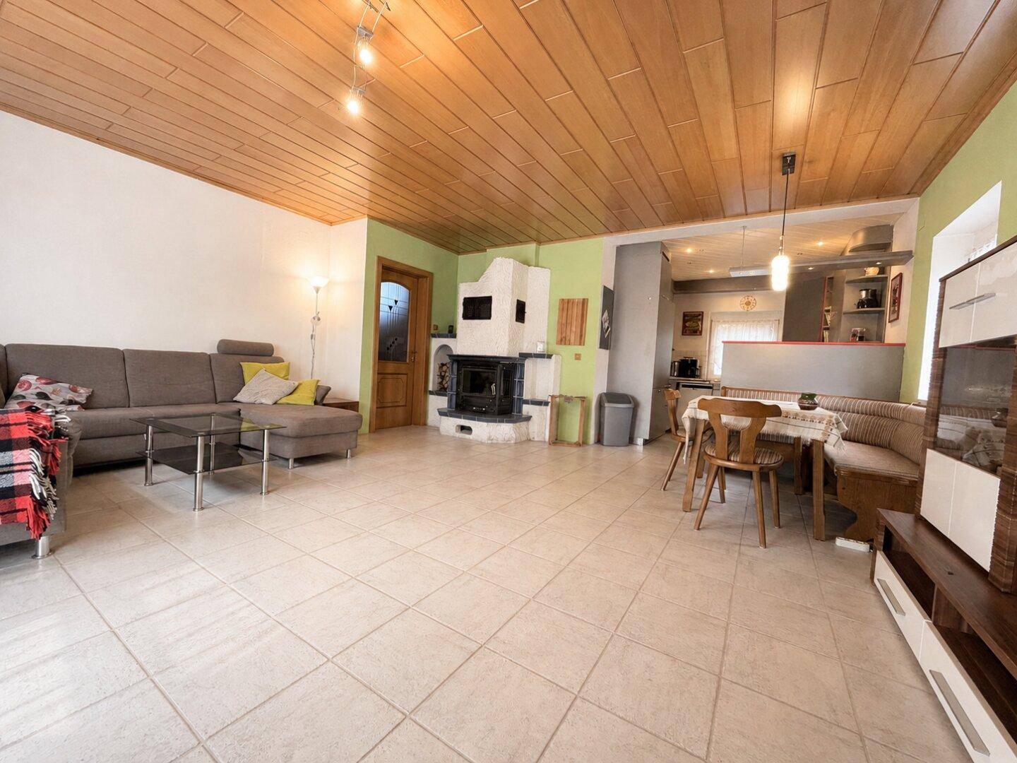 Geräumiger Wohn-Essbereich mit Kamin, Fliesenboden und einer gemütlichen Holzdecke.