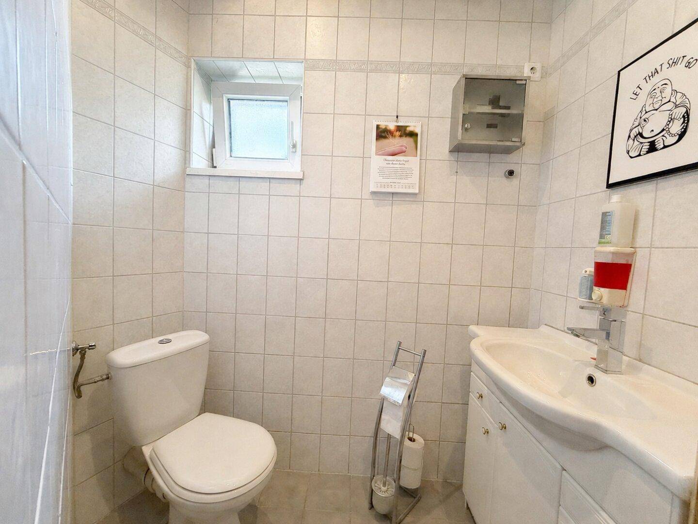 Kleines Gäste-WC mit Fenster, Toilette und Waschbecken in hell gefliestem Raum.