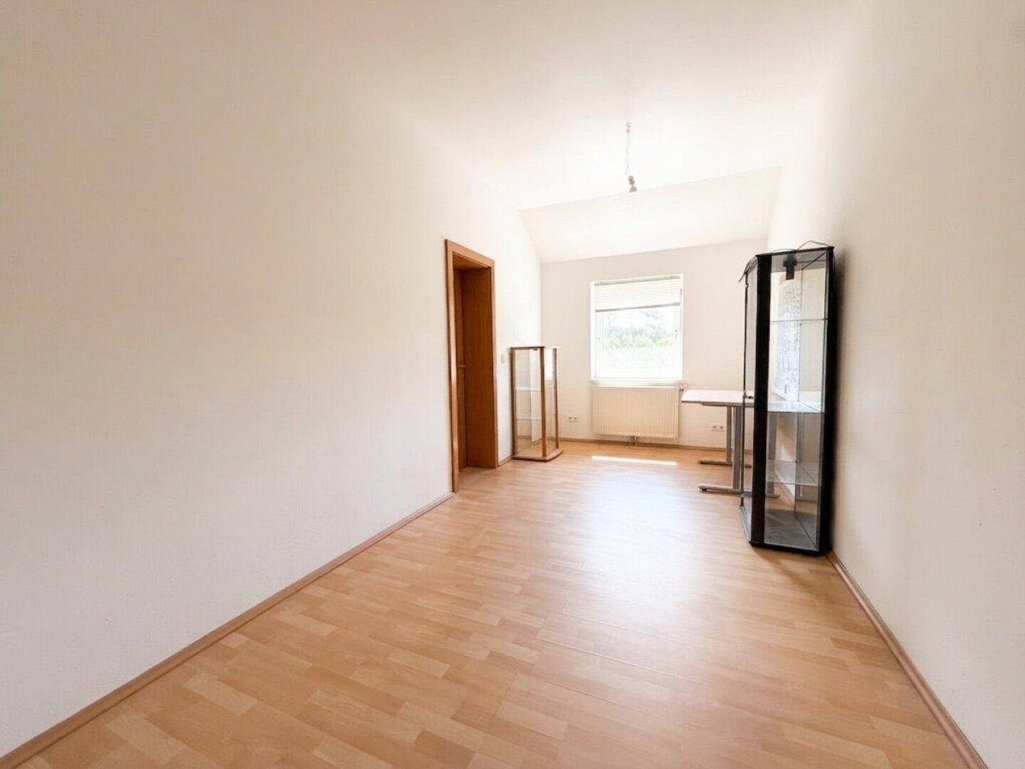 Helles Zimmer im Dachgeschoss mit Laminatboden, Dachschräge und Fenster.