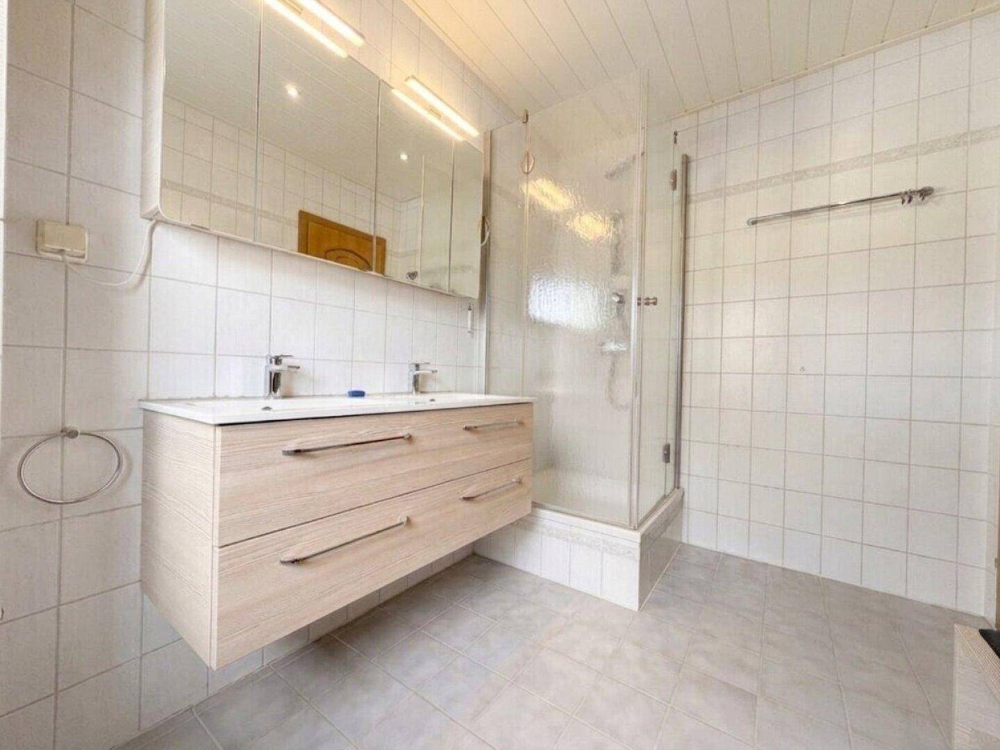 Modernes Badezimmer mit Doppelwaschbecken, Duschkabine und hellen Wandfliesen.