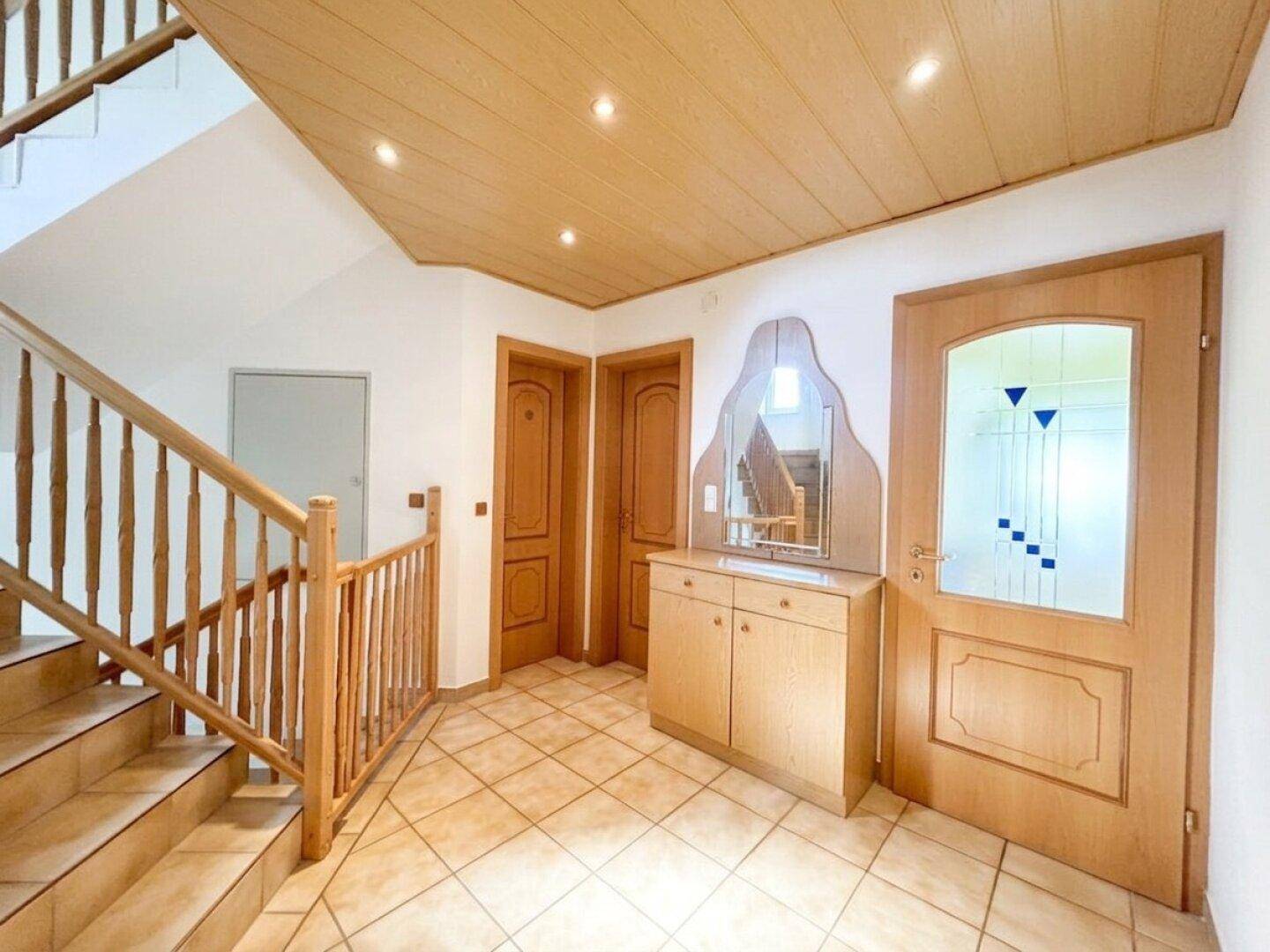 Eingangsbereich mit Holztreppe, Fliesenboden, Holzdecke und Einbauschrank mit Spiegel.