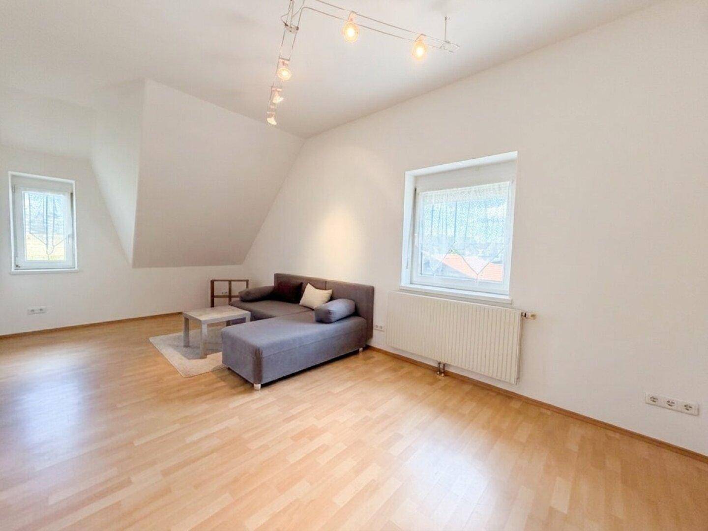 Gemütliches Wohnzimmer im Dachgeschoss mit Dachschräge, Laminatboden und Sofa.