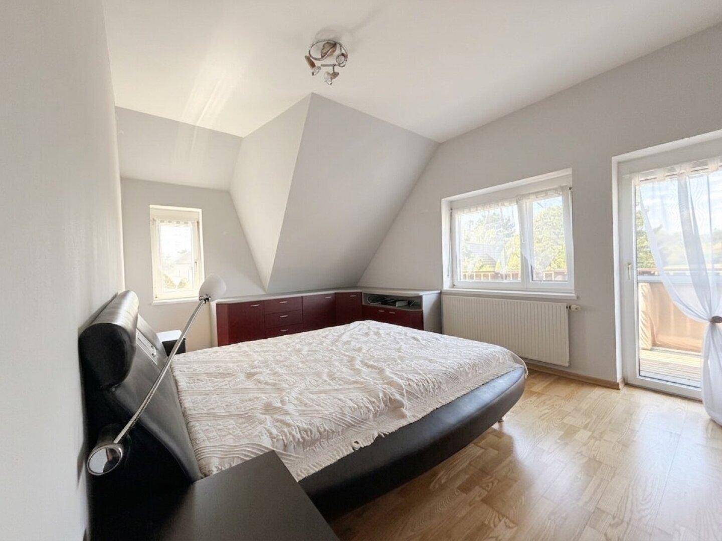 Schlafzimmer im Dachgeschoss mit Dachschräge, Laminatboden und Zugang zum Balkon.