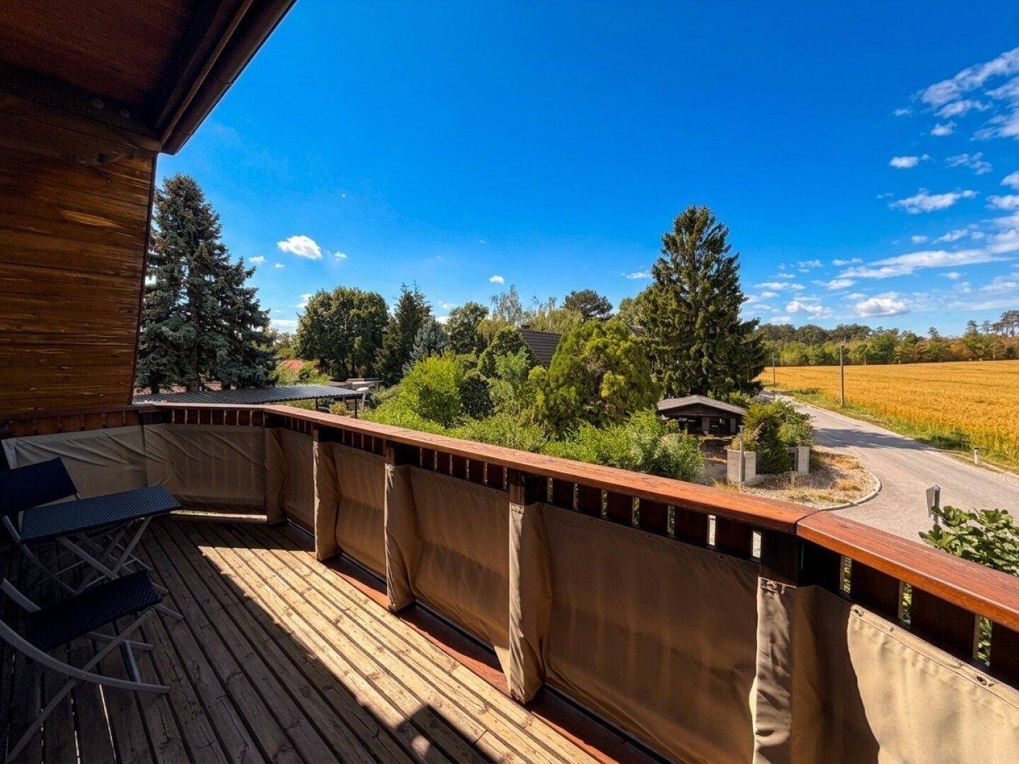 Geräumiger Balkon mit Holzboden und weitem Blick über Felder und grüne Landschaft.