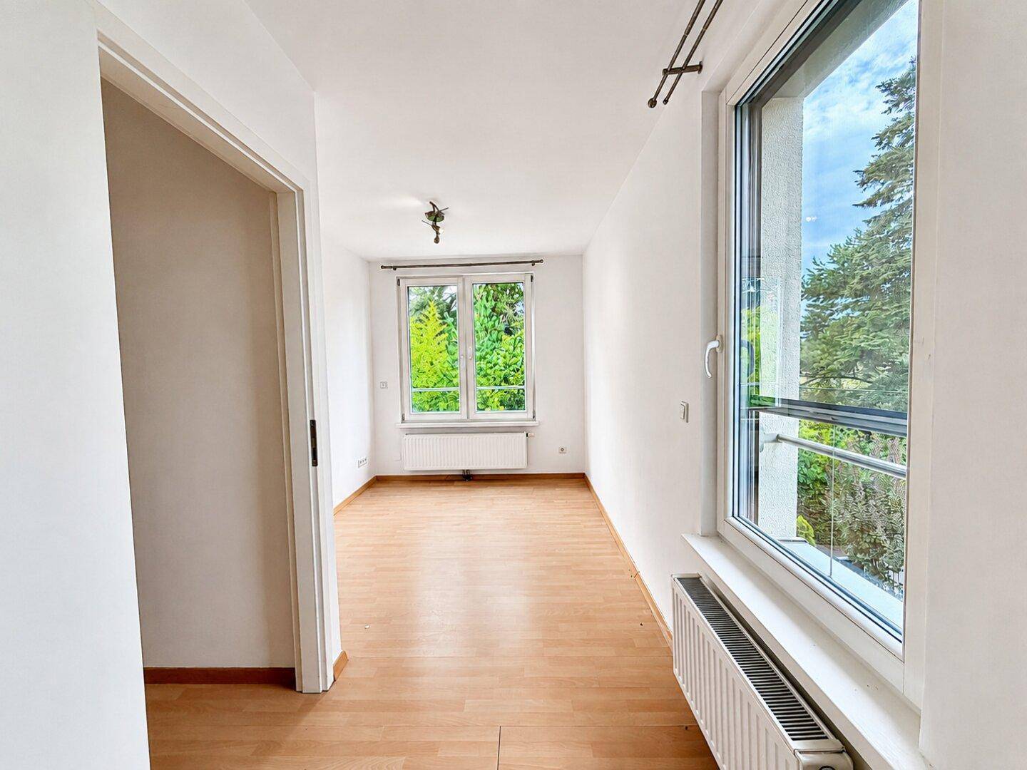 Leeres Zimmer mit Holzfußboden und großen Fenstern, ideal als Büro oder Gästezimmer.