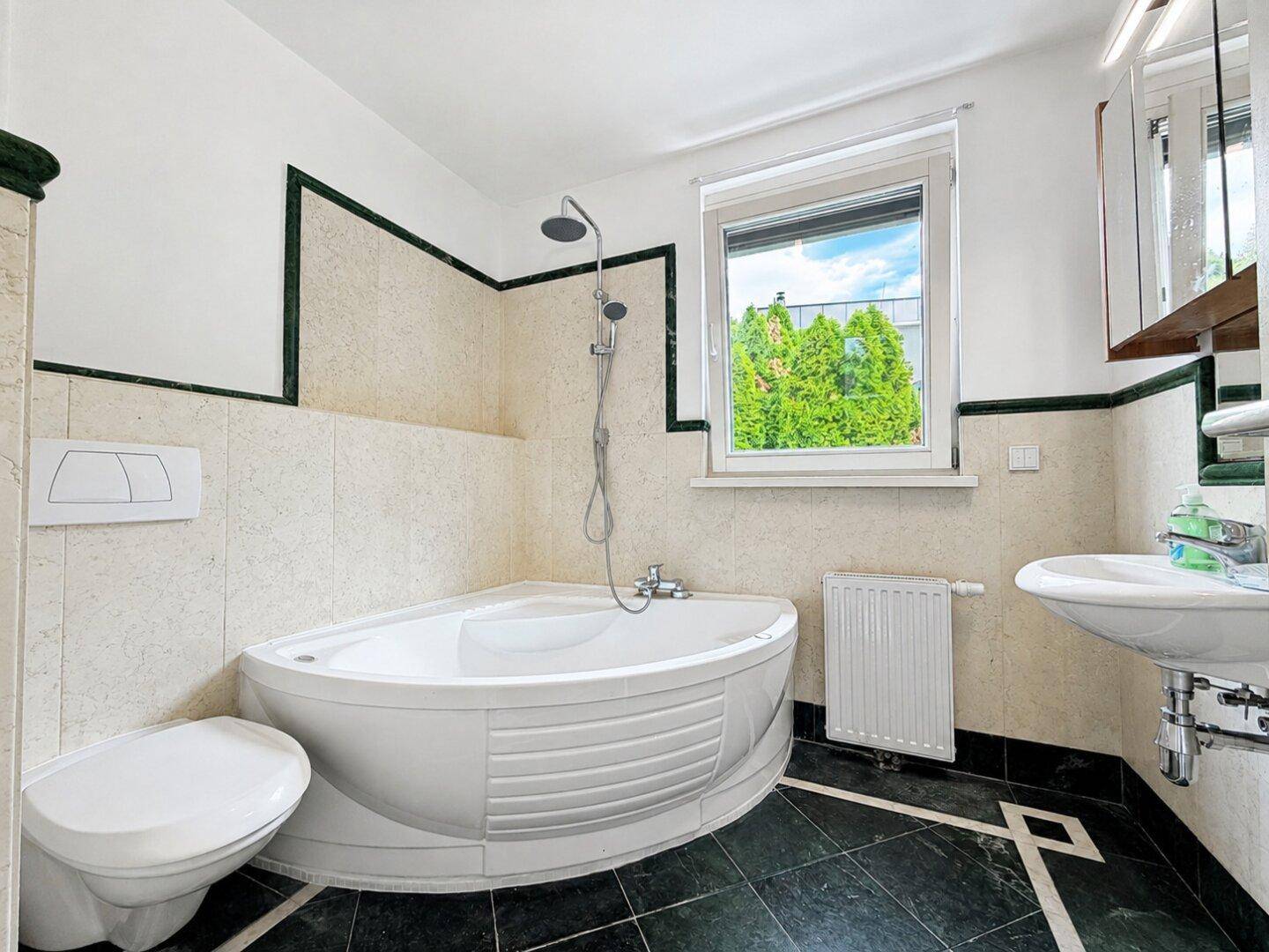 Badezimmer mit Eckbadewanne, WC und Waschbecken, ausgestattet mit Fenster für Tageslicht.
