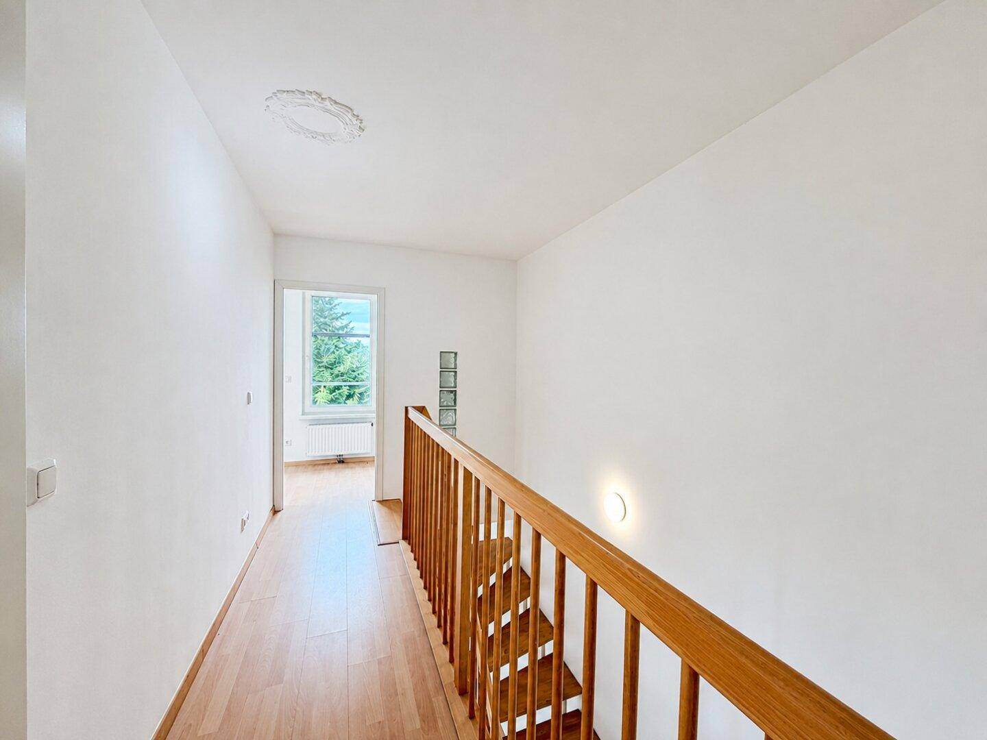 Heller Flur mit Holztreppe und Fenster, das den oberen Bereich mit Tageslicht versorgt.