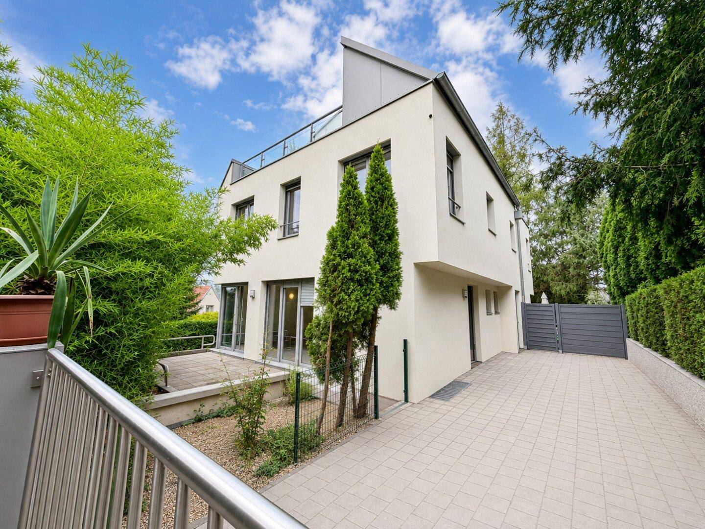 Modernes Wohnhaus mit weißer Fassade, großen Fenstern und gepflegter Außenanlage.