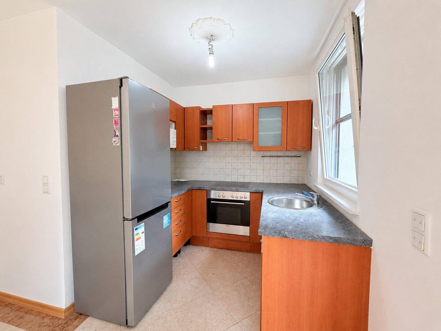 Funktionale Küche mit Holzschränken, Kühlschrank und Herd, bereit zur individuellen Gestaltung.