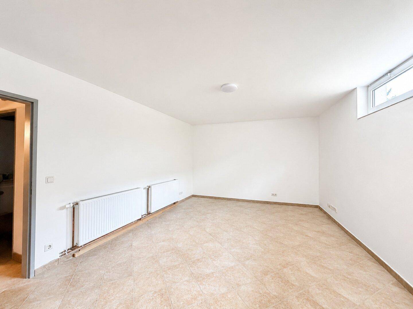 Geräumiger Raum im Untergeschoss mit Fliesenboden und kleinem Fenster, vielseitig nutzbar.