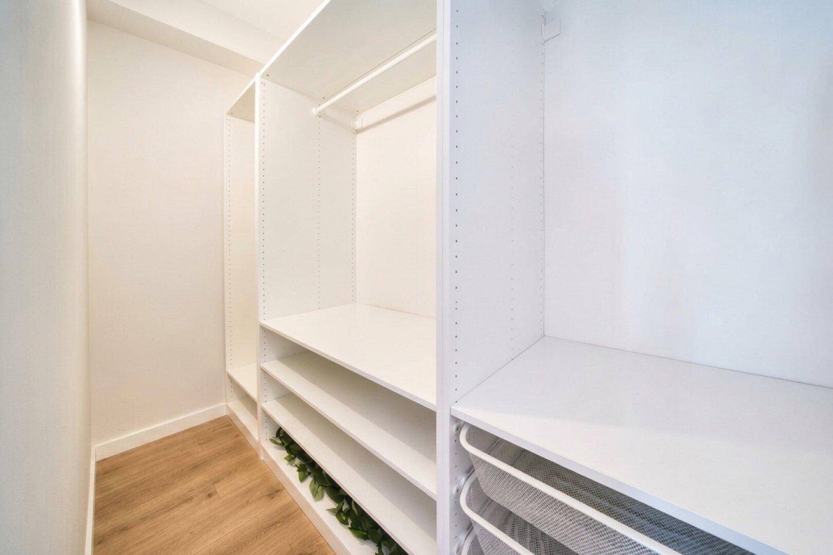 Heller begehbarer Kleiderschrank mit weißen Regalen und praktischen Aufbewahrungslösungen.