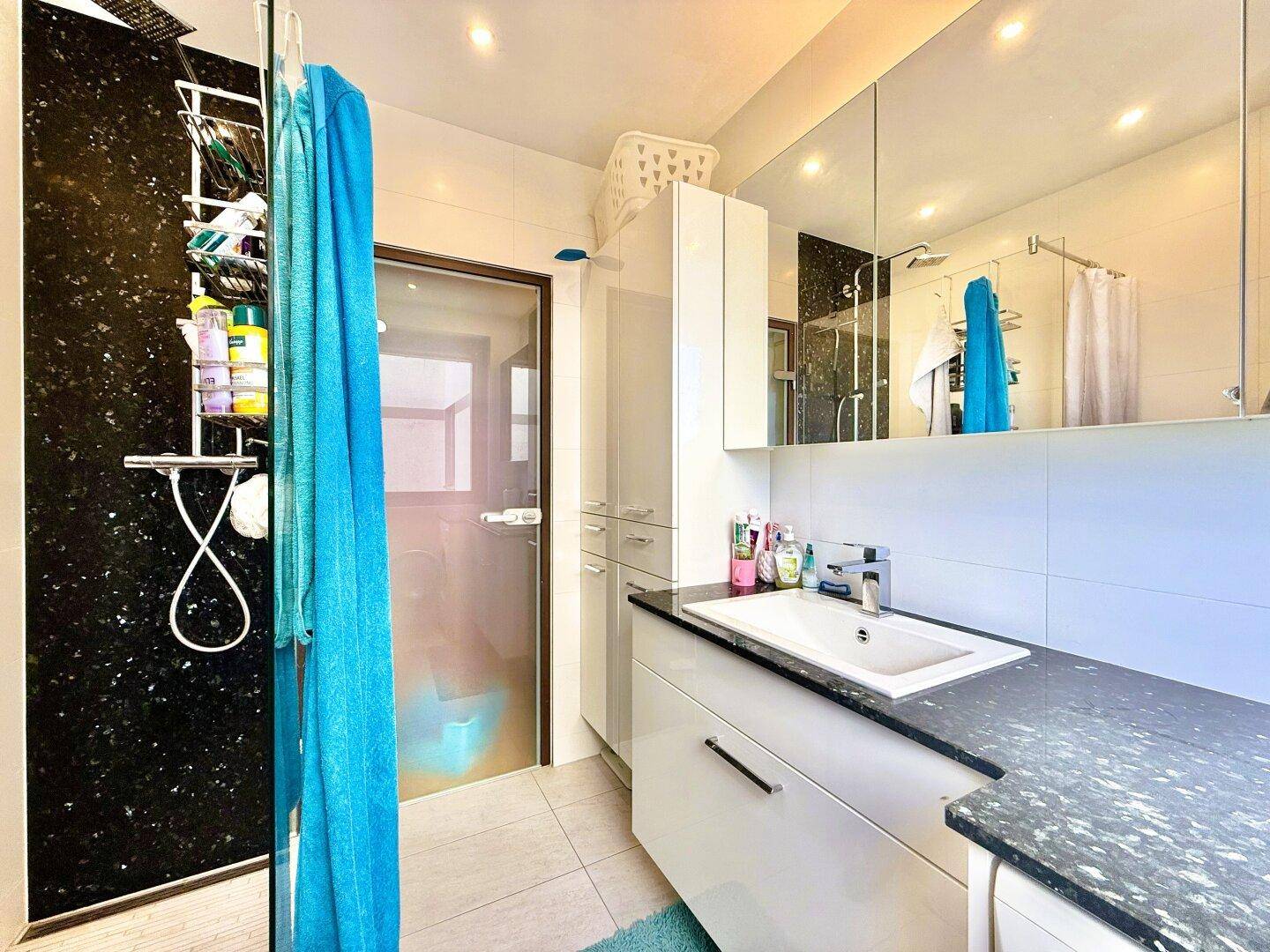 Modernes Badezimmer mit Dusche, Einzelwaschbecken und großem Spiegelschrank.
