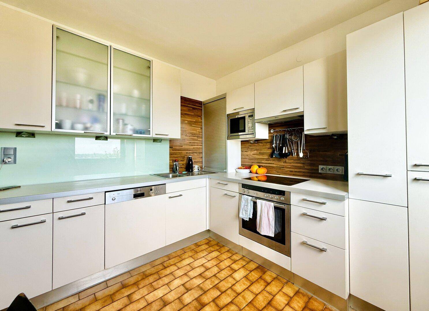 Moderne Einbauküche mit weißen Schränken, integrierten Geräten und Fliesenboden.