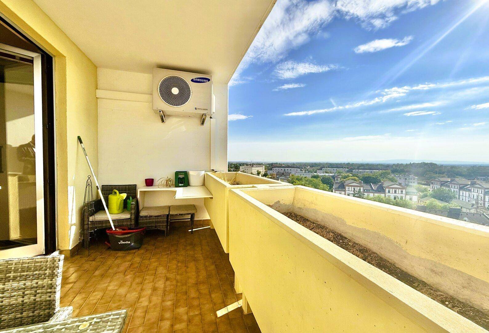 Heller Balkon mit Klimaanlage, Pflanzkästen und weitem Blick über die Stadt.
