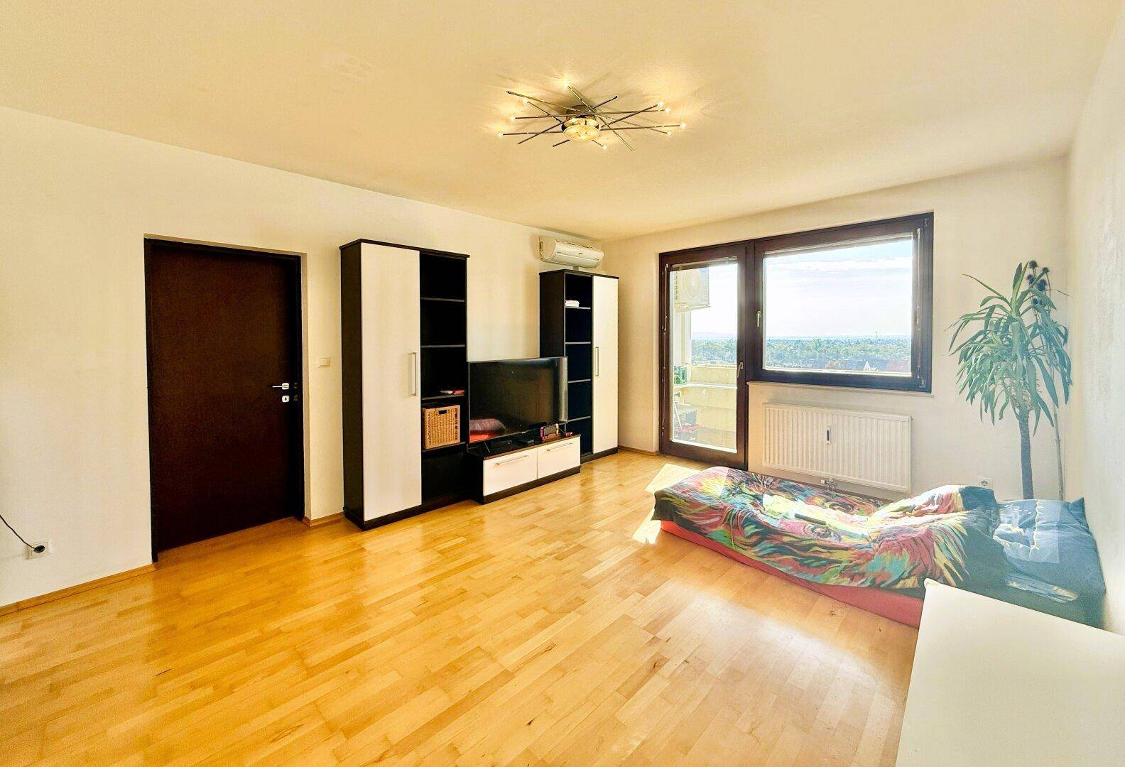 Geräumiges Wohnzimmer mit hellem Holzfußboden, TV-Möbel und großem Fenster.