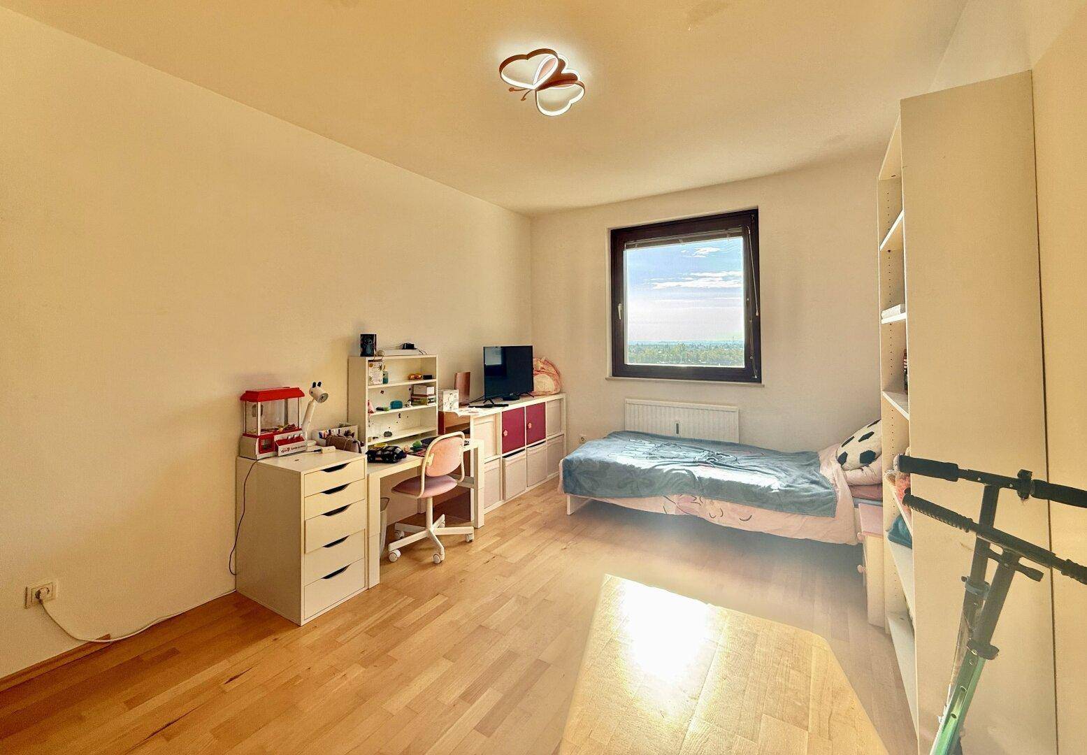 Kinderzimmer mit hellem Holzfußboden, Schreibtisch und einem Fenster.