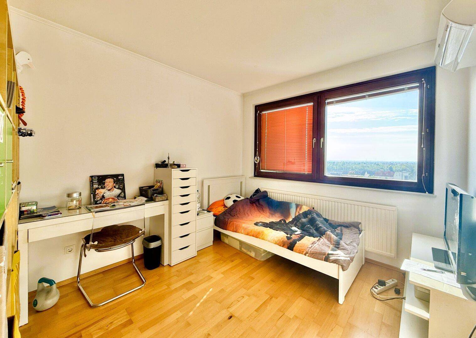 Helles Schlafzimmer mit Einzelbett, Schreibtisch und Fenster mit weitem Ausblick.