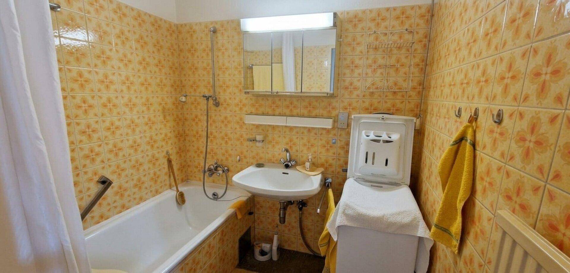 Ein Badezimmer im Stil der 80er Jahre mit orange gemusterten Fliesen und Badewanne.