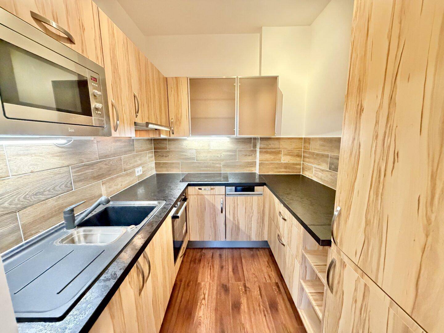 Moderne Einbauküche mit Holzfronten, dunklen Arbeitsplatten und integrierten Geräten.