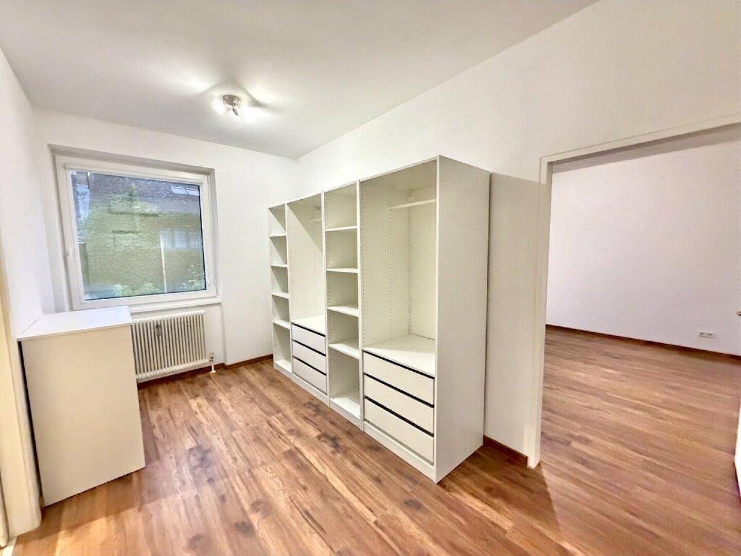 Zimmer mit Holzfußboden, Fenster und einem großen, offenen Kleiderschranksystem.