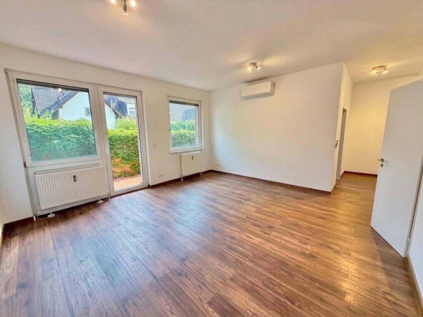 Heller Wohnraum mit Holzfußboden, Klimaanlage und Zugang zu einem Außenbereich.