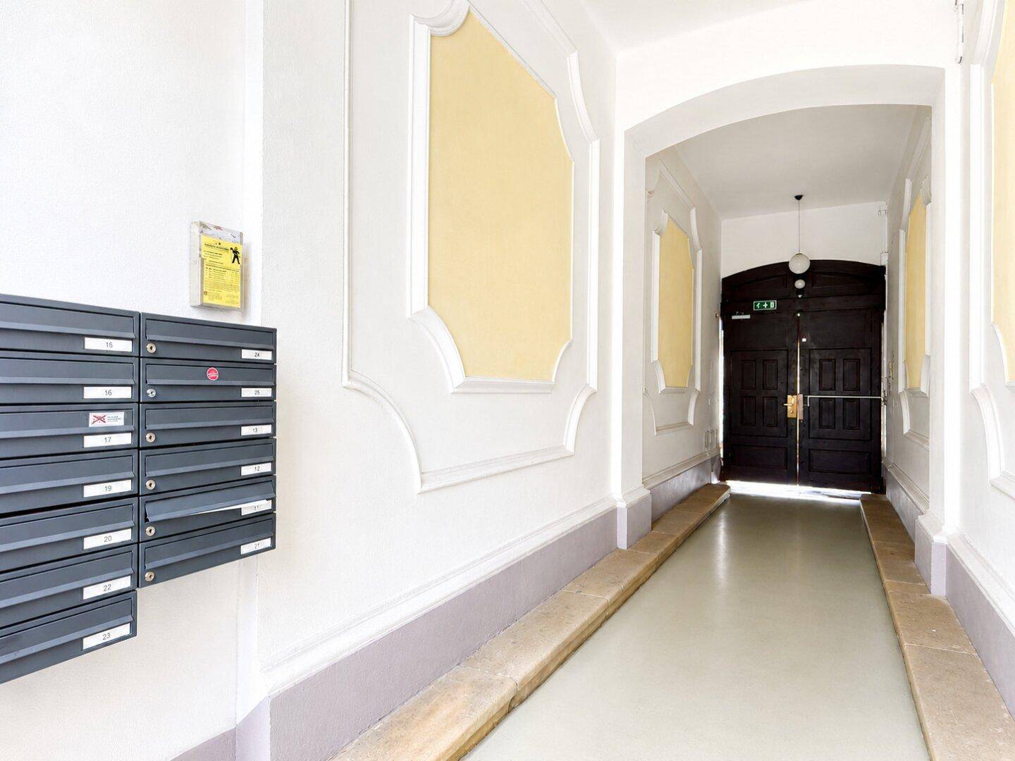 Eingangsbereich eines Mehrfamilienhauses mit Briefkästen und barrierefreier Rampe.