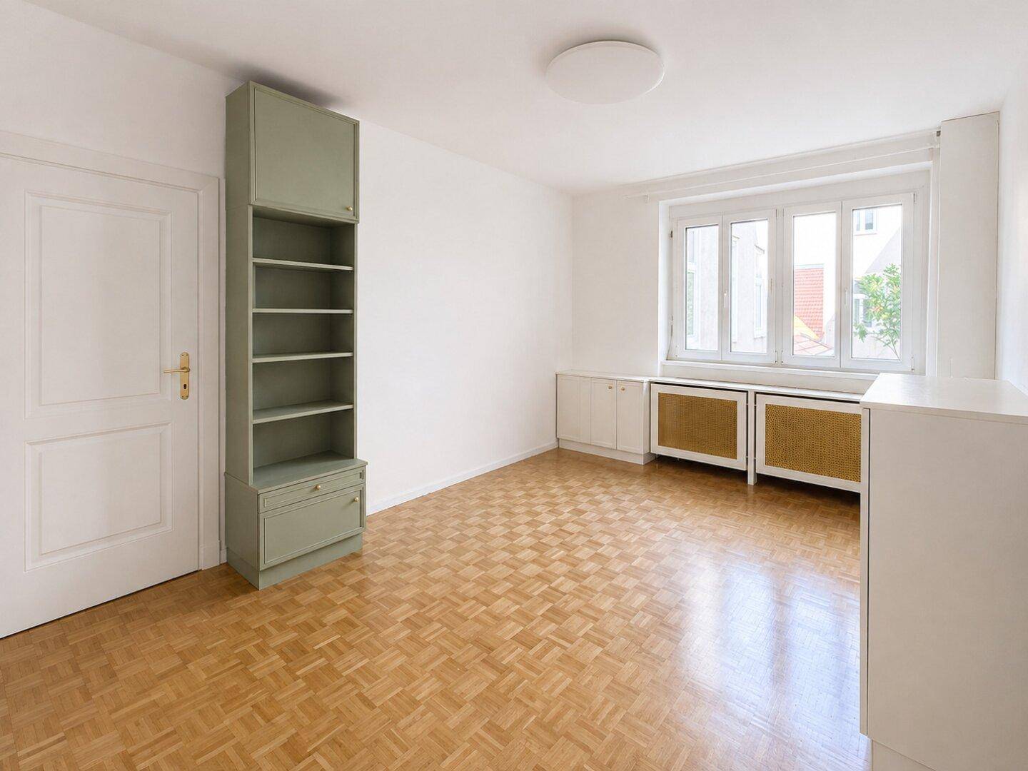Leeres Zimmer mit Parkettboden, Einbauregal und Fenster mit Rollläden.