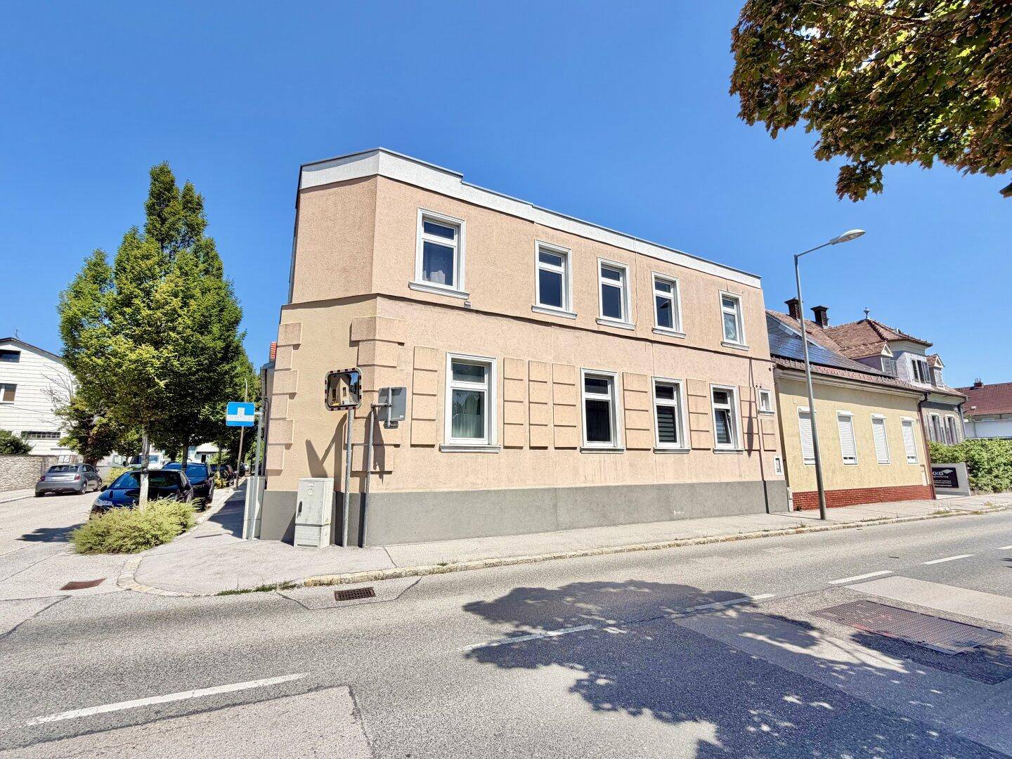 Eckansicht eines Mehrfamilienhauses mit beiger Fassade und vielen Fenstern an einer Straße.