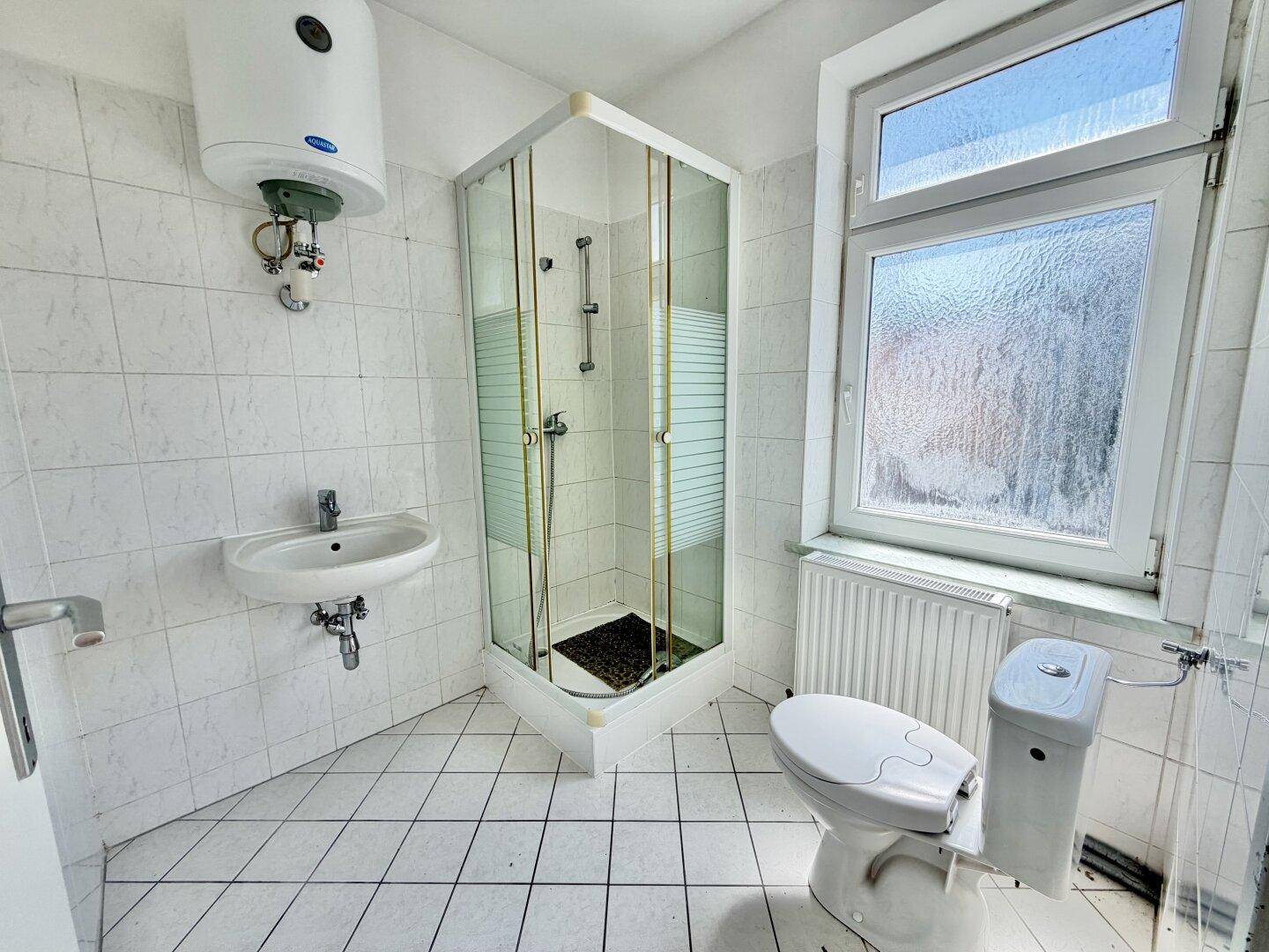 Helles Badezimmer mit weiß gefliesten Wänden, Dusche, Toilette und Waschbecken.