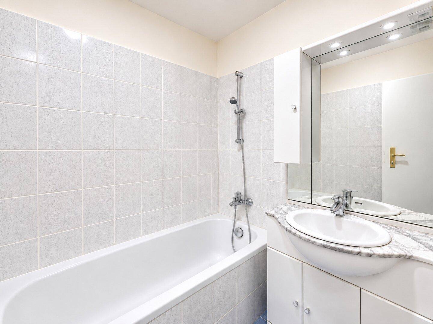 Badezimmer mit Badewanne, Waschtisch mit Marmorplatte und hellgrauen Wandfliesen.