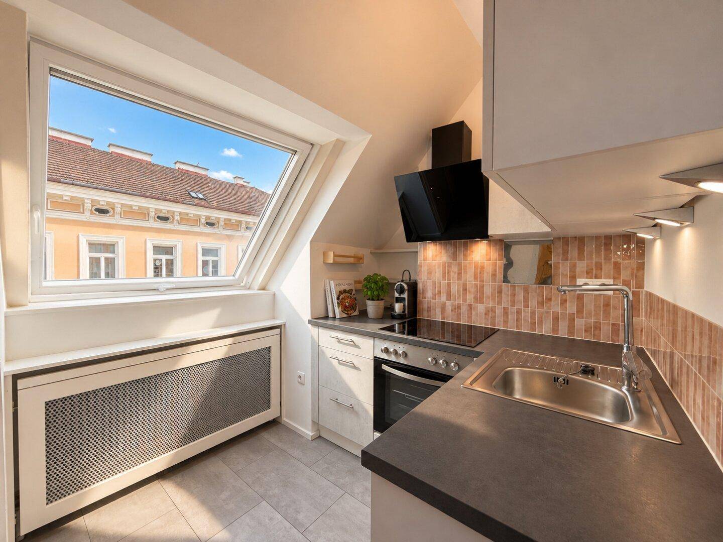 Moderne Küche mit Dachschräge, Dachfenster, Einbaugeräten und dunkler Arbeitsplatte, hell gefliest.
