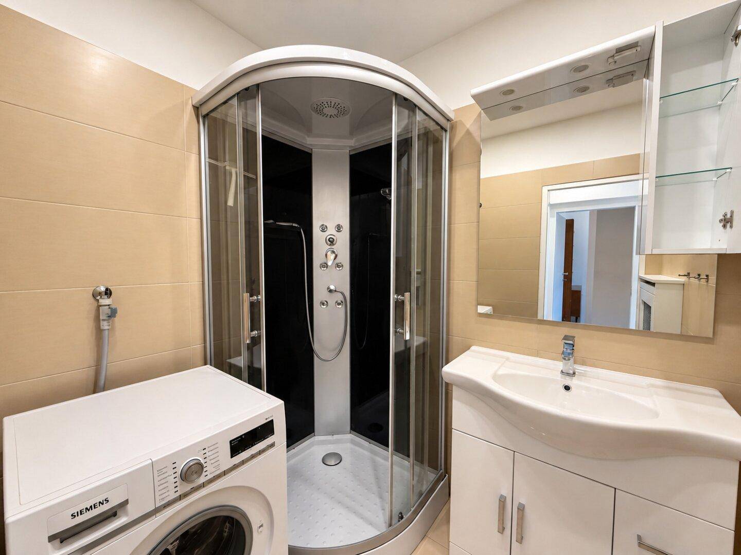 Funktionales Badezimmer mit Duschkabine, Waschbecken, Spiegelschrank und hellen Fliesen.