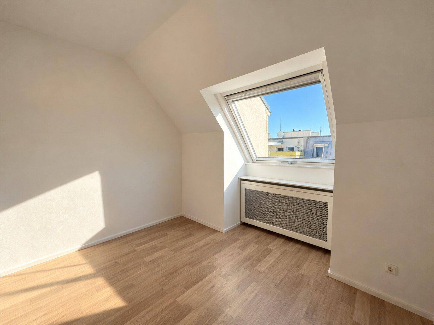 Unmöbliertes Schlafzimmer mit Dachschräge, großem Dachfenster und Holzboden, bereit zur individuellen Gestaltung.