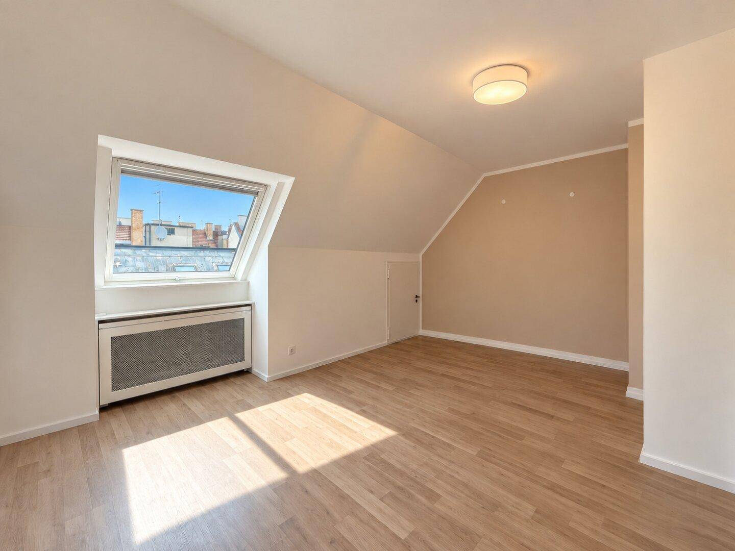 Heller, unmöblierter Raum mit Dachschräge, großem Dachfenster und Holzboden, ideal als Wohnzimmer.