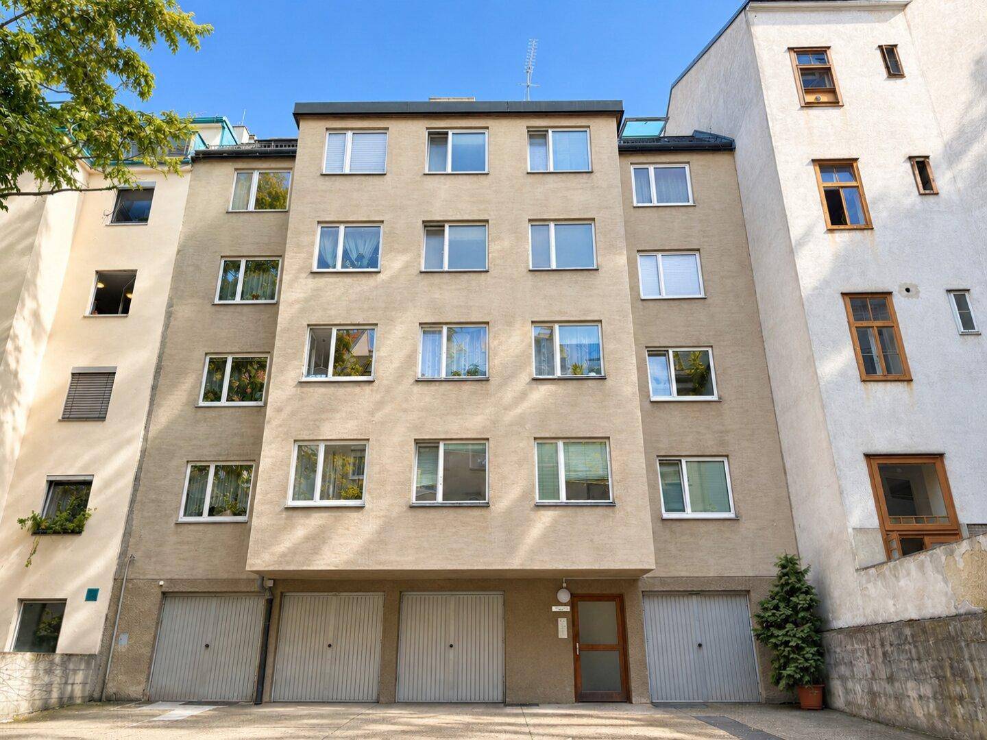 Mehrfamilienhausfassade mit mehreren Etagen, zahlreichen Fenstern und Garagen im Erdgeschoss.