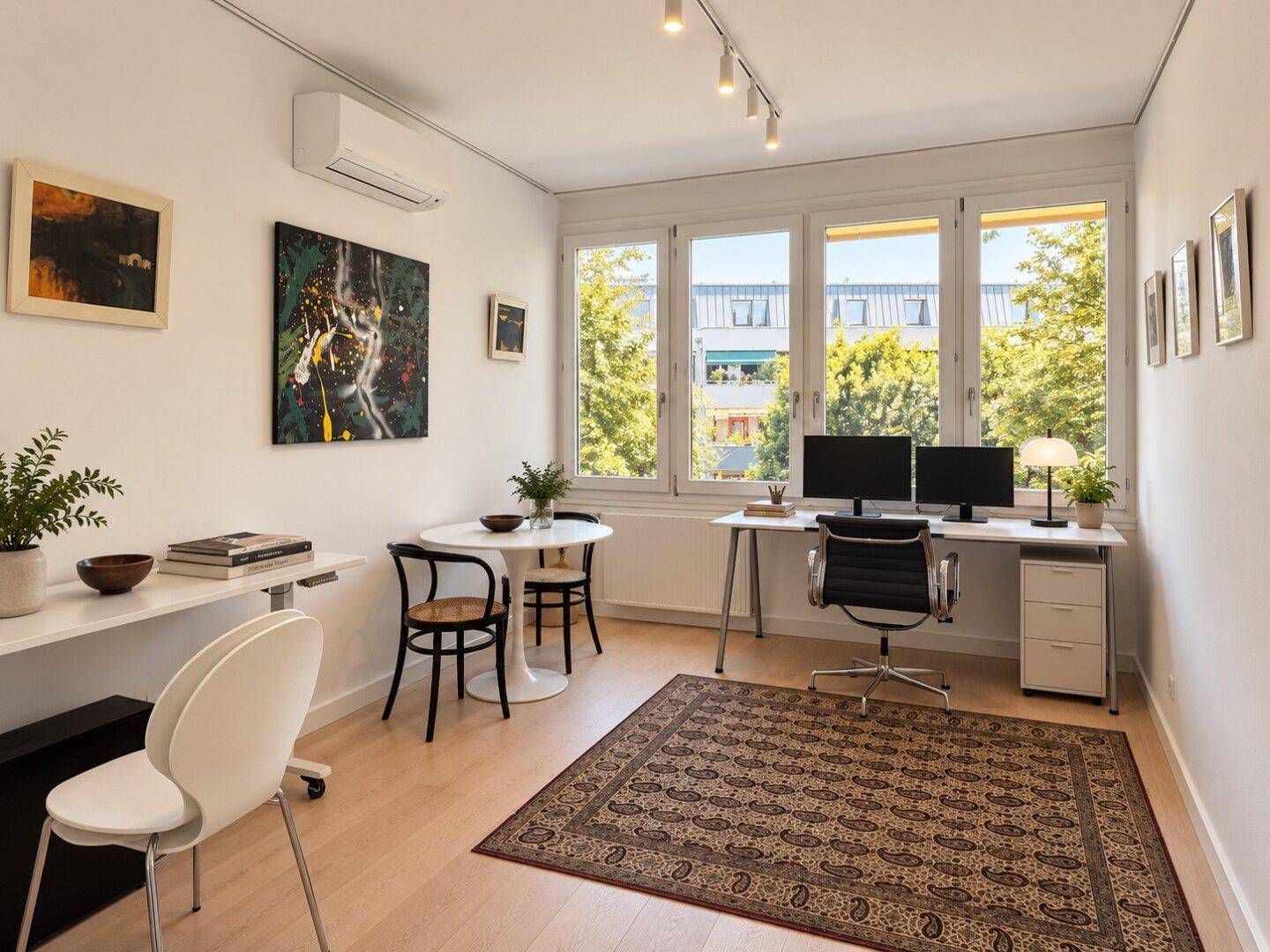 Helles Arbeitszimmer mit zwei Schreibtischen, Holzboden und großen Fenstern mit Blick ins Grüne.