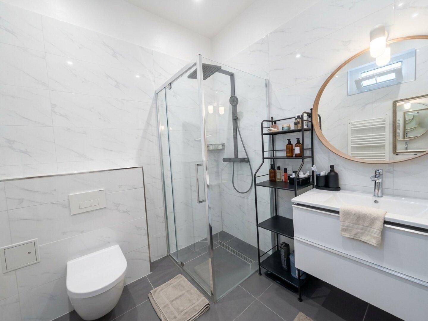 Modernes Badezimmer mit weißen Marmorfliesen, ebenerdiger Dusche und Waschtisch mit Spiegel.