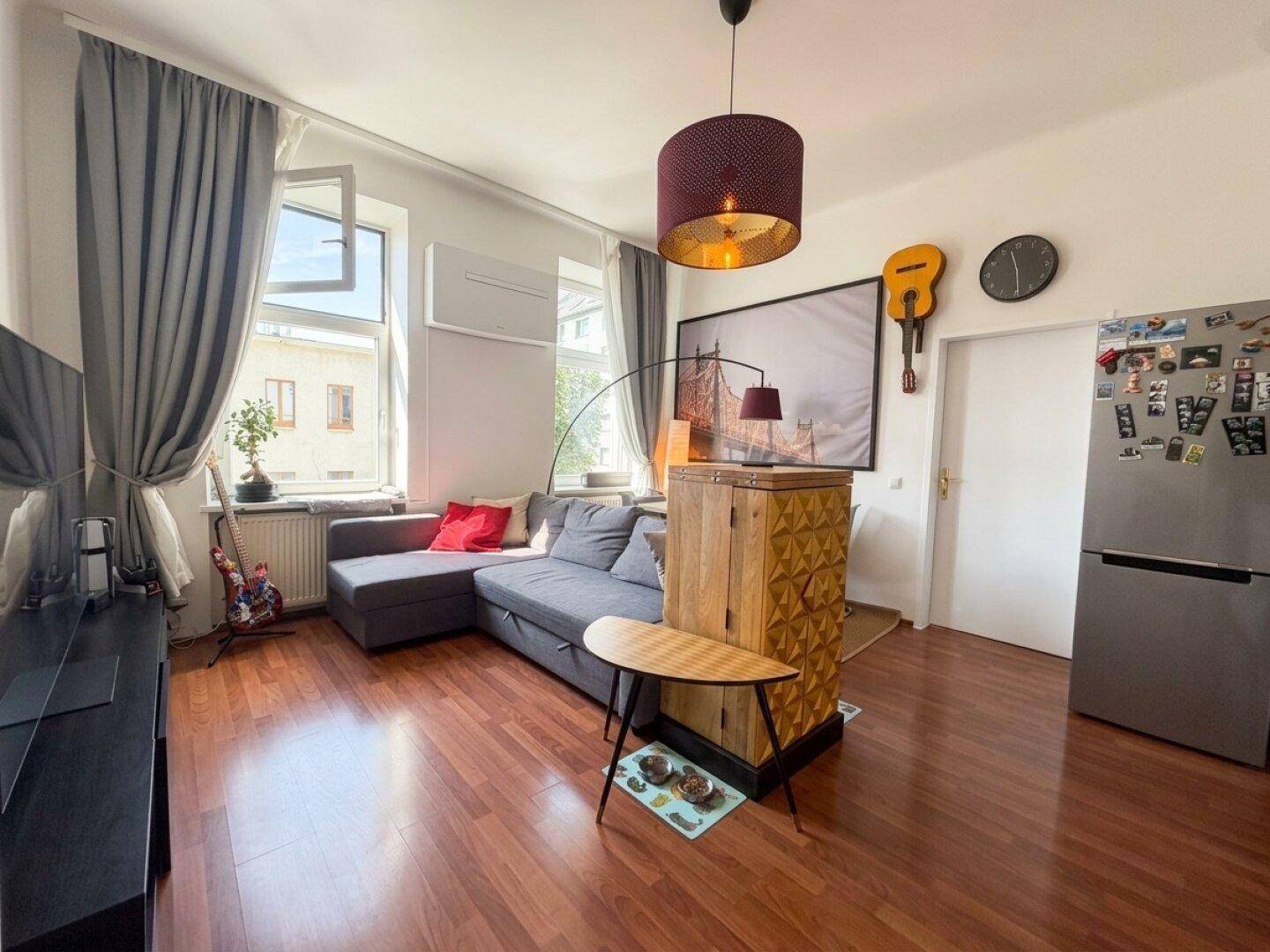 Gemütliches Wohnzimmer mit grauem Ecksofa, Holzboden und Klimaanlage.