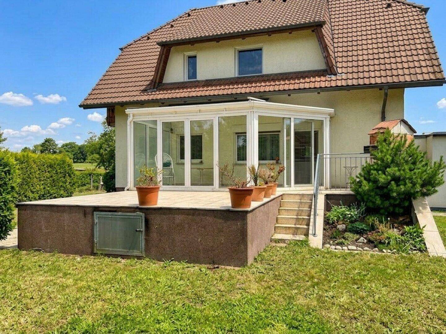 Haus mit hellem Wintergarten, großer Terrasse und gepflegtem Gartenbereich.