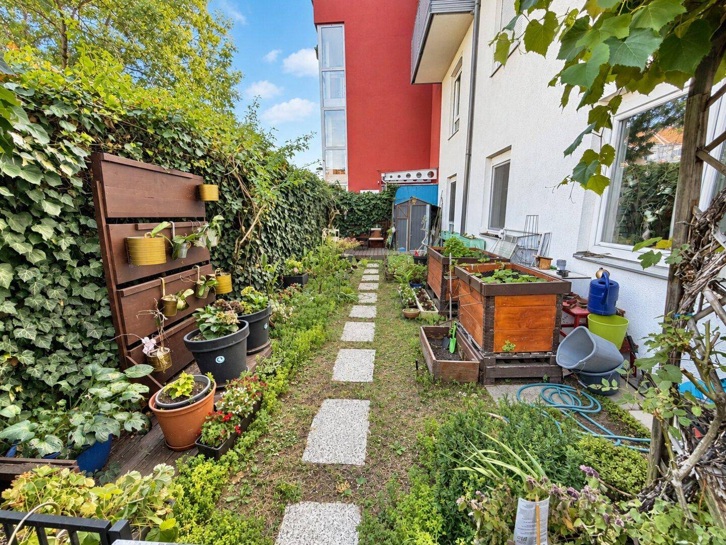 Gepflegter Gartenbereich mit Hochbeeten und einem kleinen Pfad, umgeben von grünen Pflanzen.