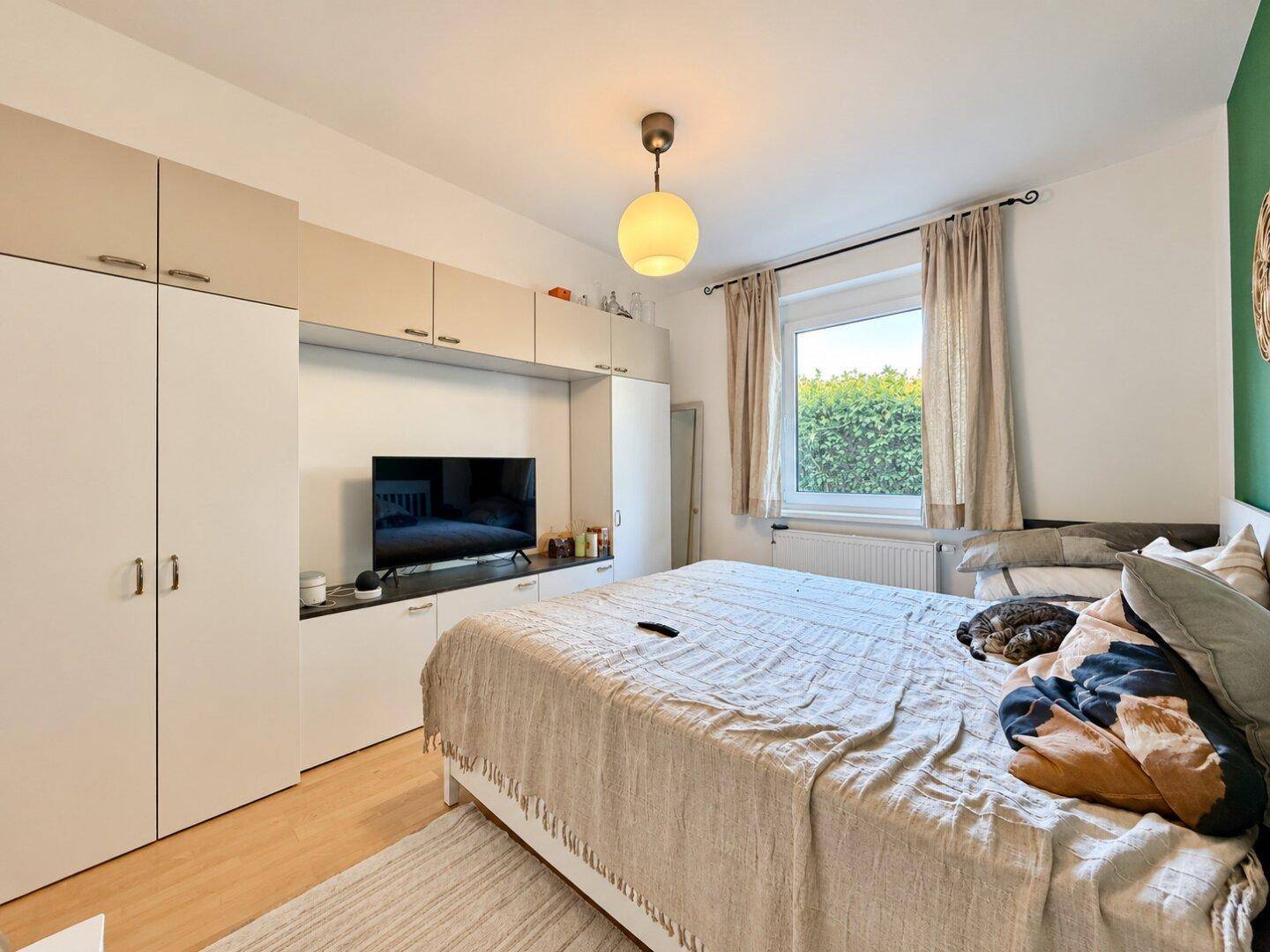 Gemütliches Schlafzimmer mit Doppelbett, Einbauschränken und Blick ins Grüne durch das Fenster.