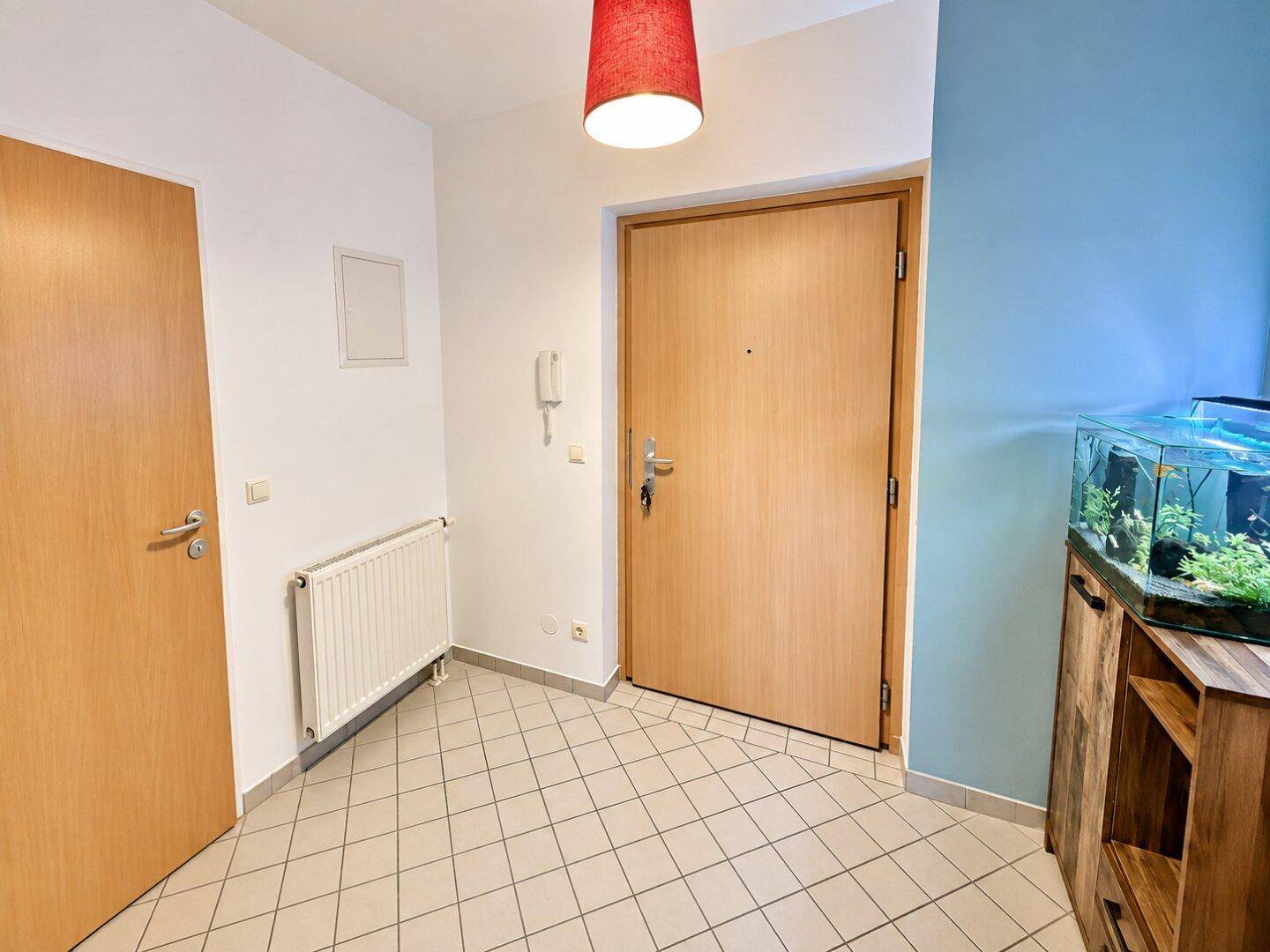 Eingangsbereich mit Fliesenboden, Holztüren und einem dekorativen Aquarium auf einem Schrank.
